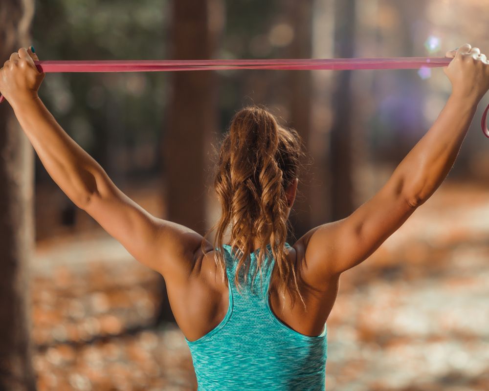 Una mujer de espaldas entrenando con una goma de resistencia.
